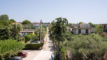 A residential street with houses, a parked car, and lush greenery.