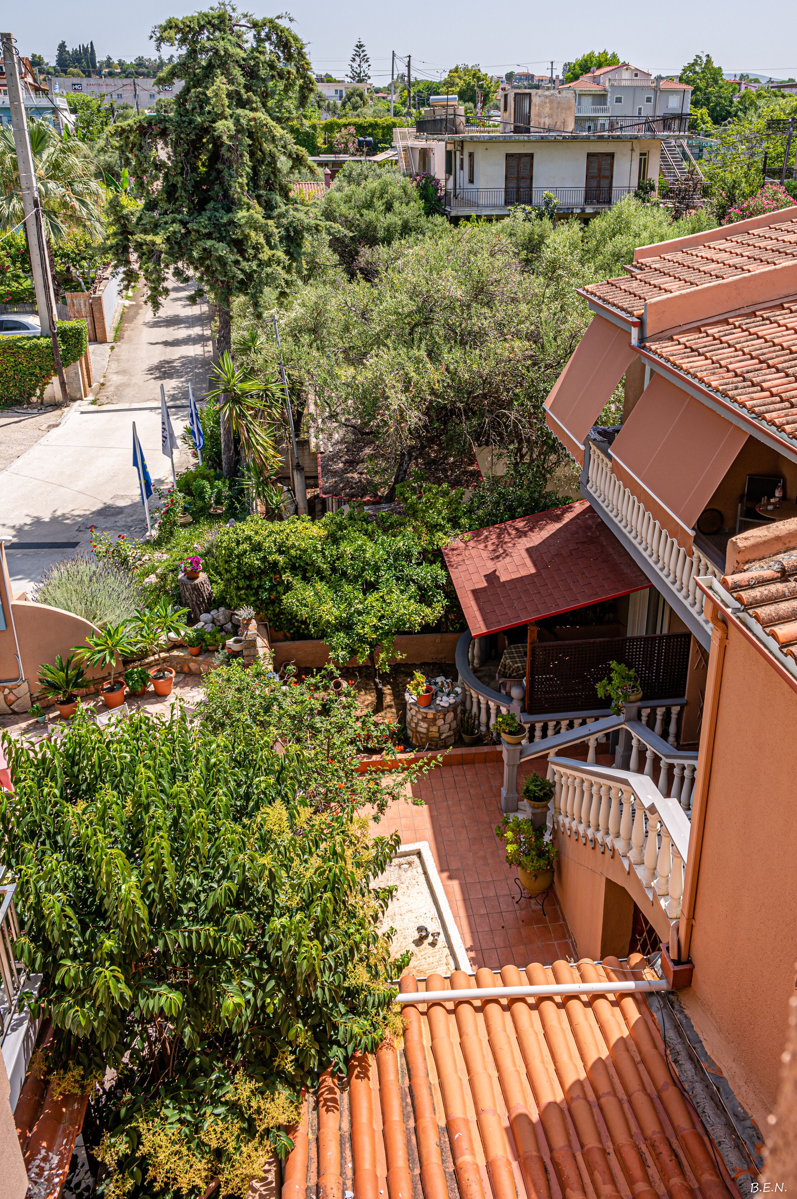 Ein Wohngebiet mit einem Haus, das ein rotes Ziegeldach, einen Balkon und einen Garten mit verschiedenen Pflanzen hat.