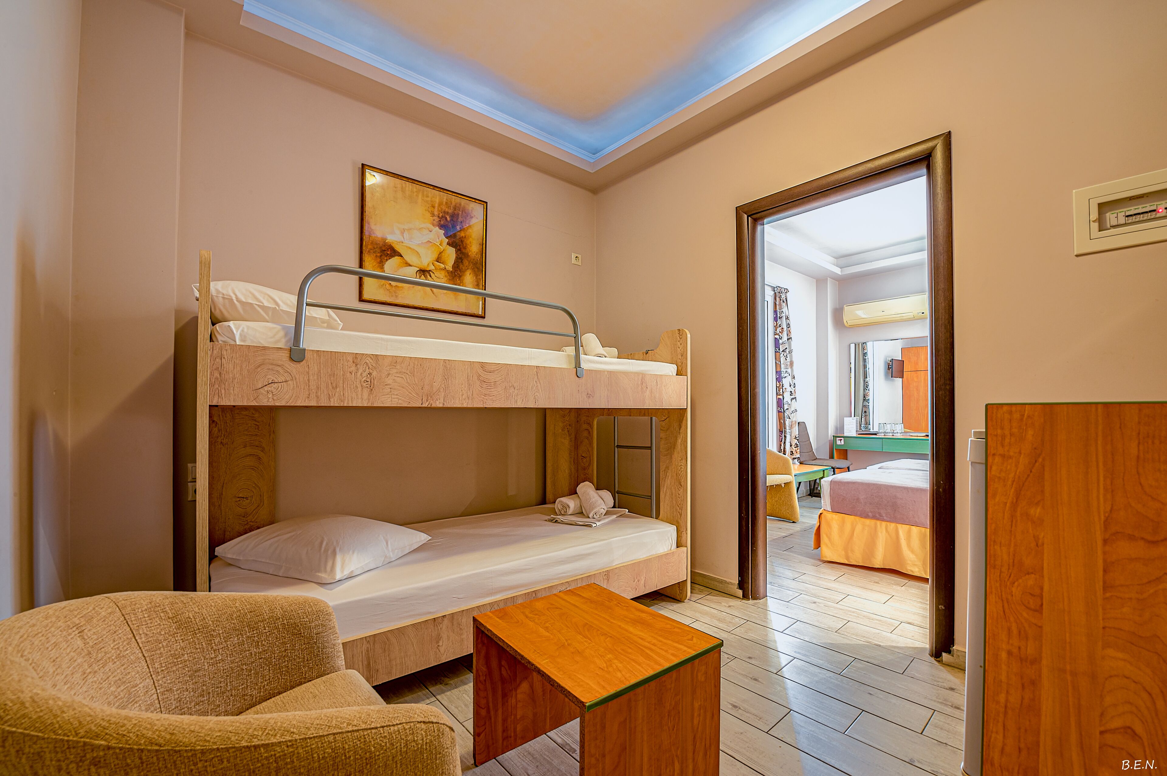A bunk bed room with a painting, a desk, and a door leading to another room.