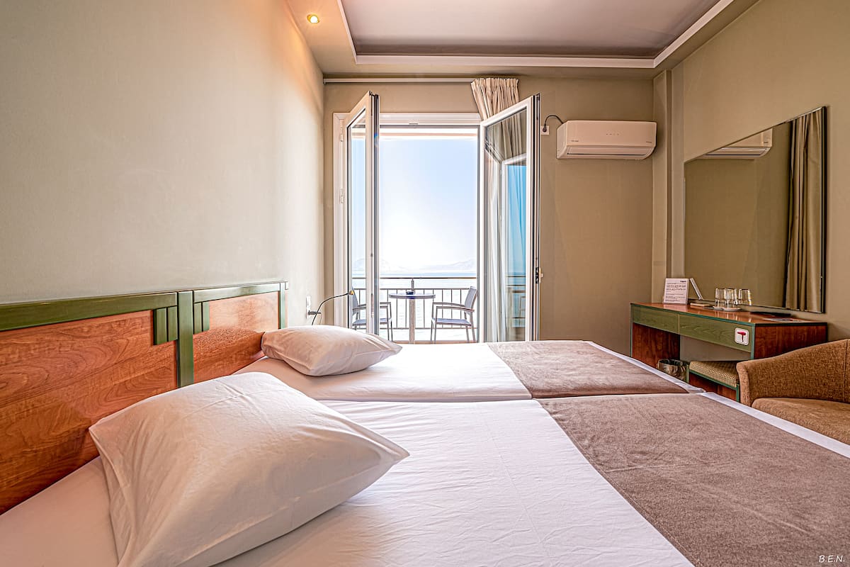 Quarto de hotel com duas camas, uma mesa pequena, uma cadeira, um espelho e um aparelho de ar condicionado.