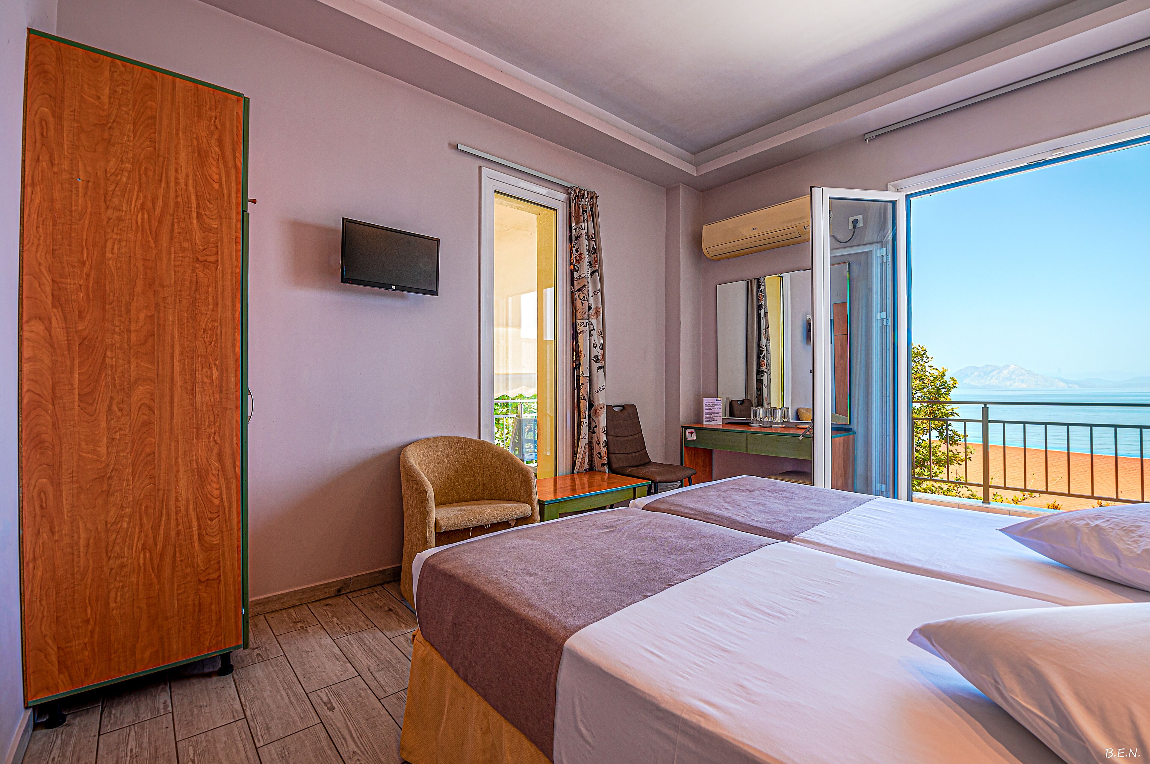 A hotel room with a bed, a chair, a desk, a television, and a balcony with a view of the sea.