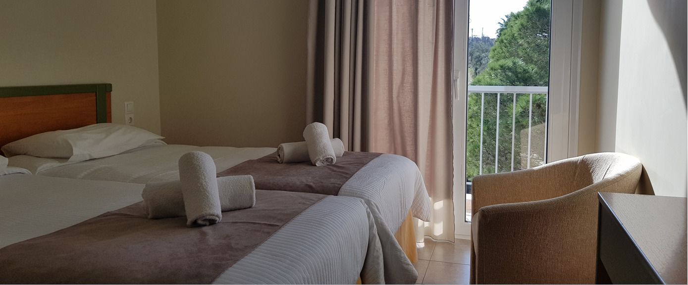 Habitación de hotel con dos camas, una silla y un balcón con cortinas.