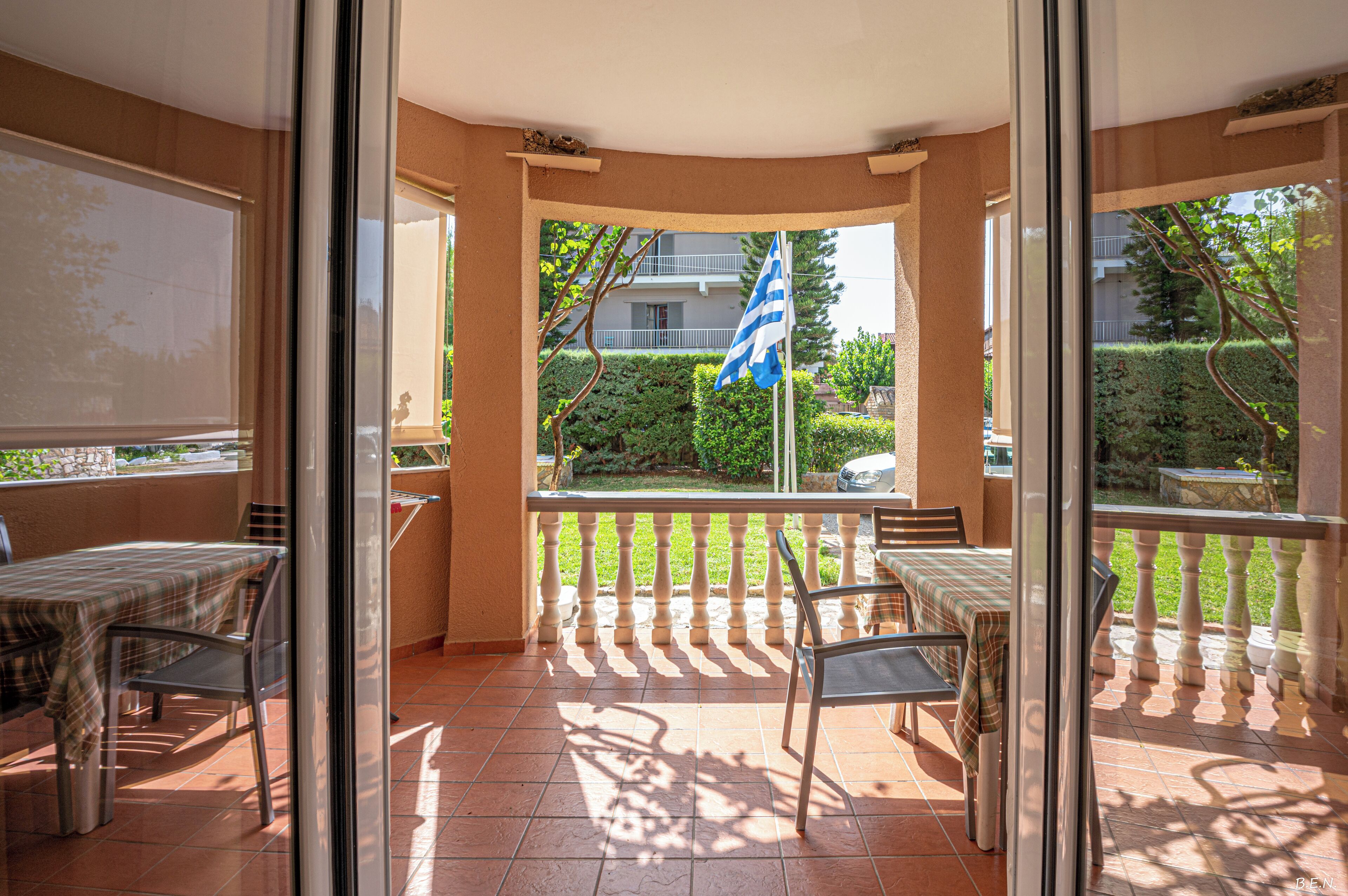 Un balcón con mesa y sillas, una bandera y vista a una zona residencial.
