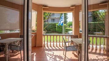 Un balcón con mesa y sillas, una bandera y vista a una zona residencial.