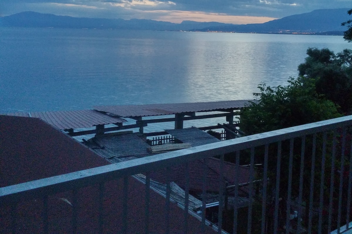 Vista costeira com um deck de madeira sobre um mar calmo e montanhas ao longe.