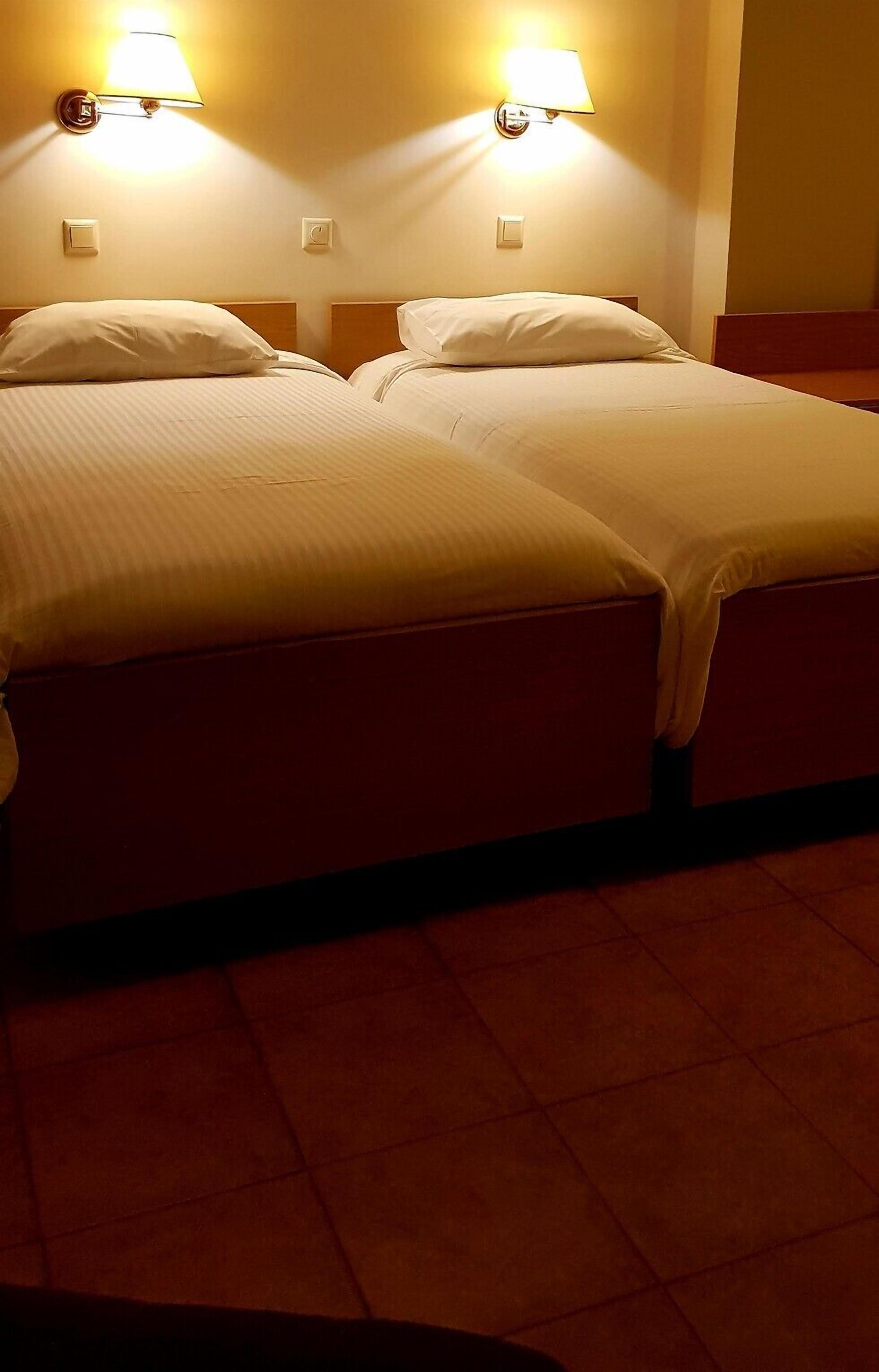 Habitación de hotel con dos camas, cada una con cabecera y lámpara de noche.