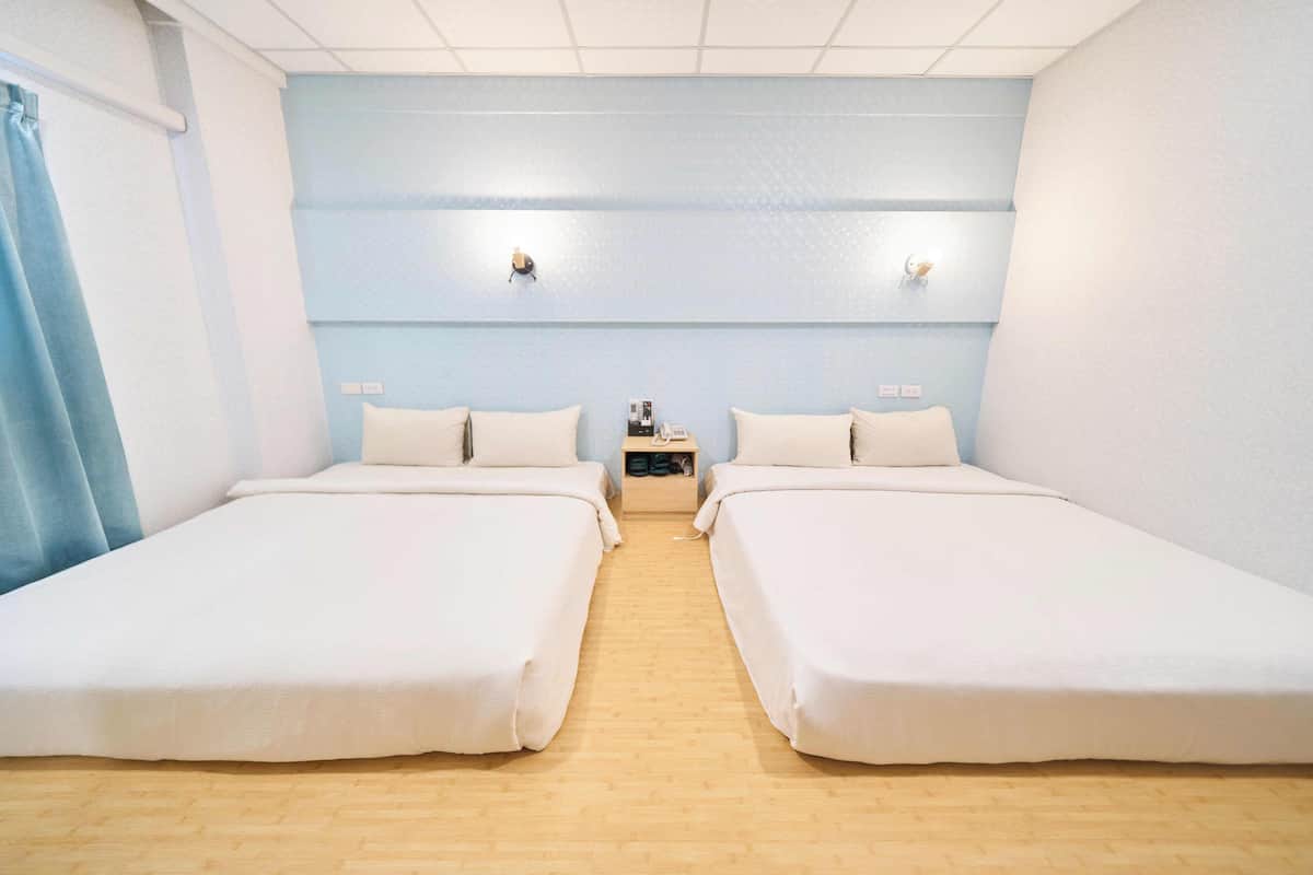 Une chambre avec deux lits simples, un plancher en bois, des murs bleu clair et une petite table avec une lampe et un téléphone.