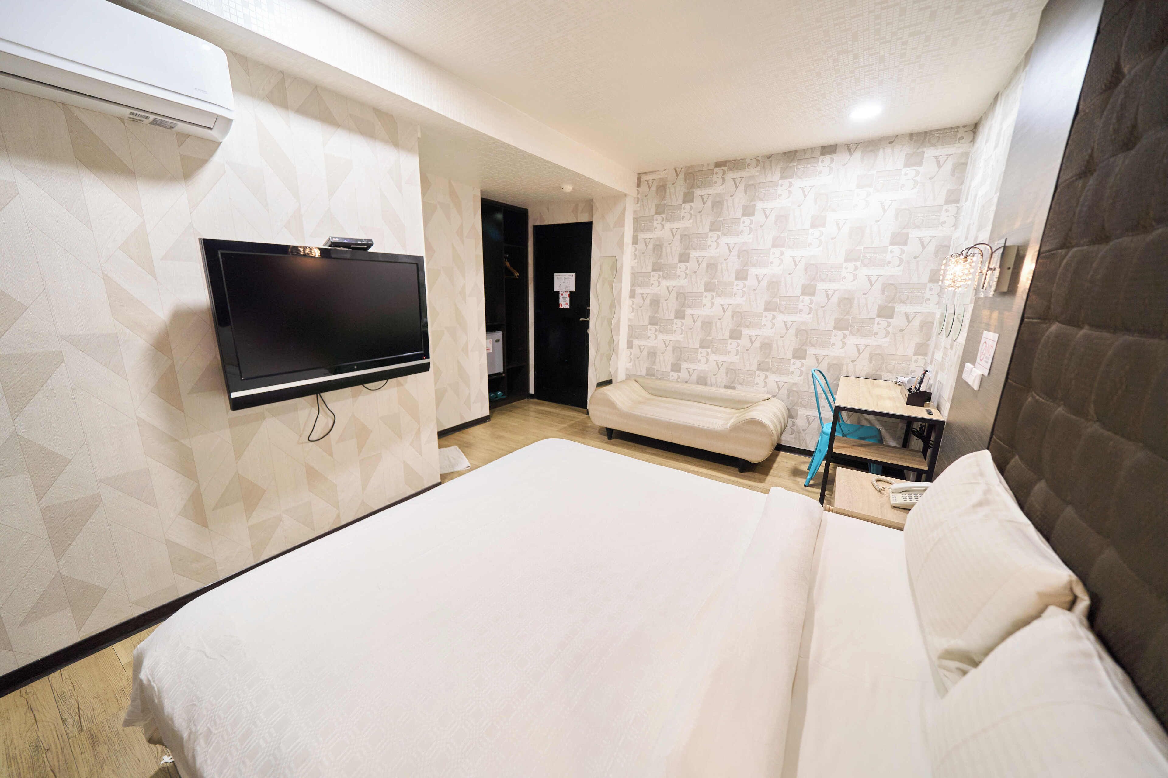 A hotel room with a large bed, a flat-screen TV mounted on the wall, a bedside table, and a bathroom with a mirror and sink.