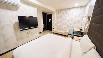 A hotel room with a large bed, a flat-screen TV mounted on the wall, a bedside table, and a bathroom with a mirror and sink.