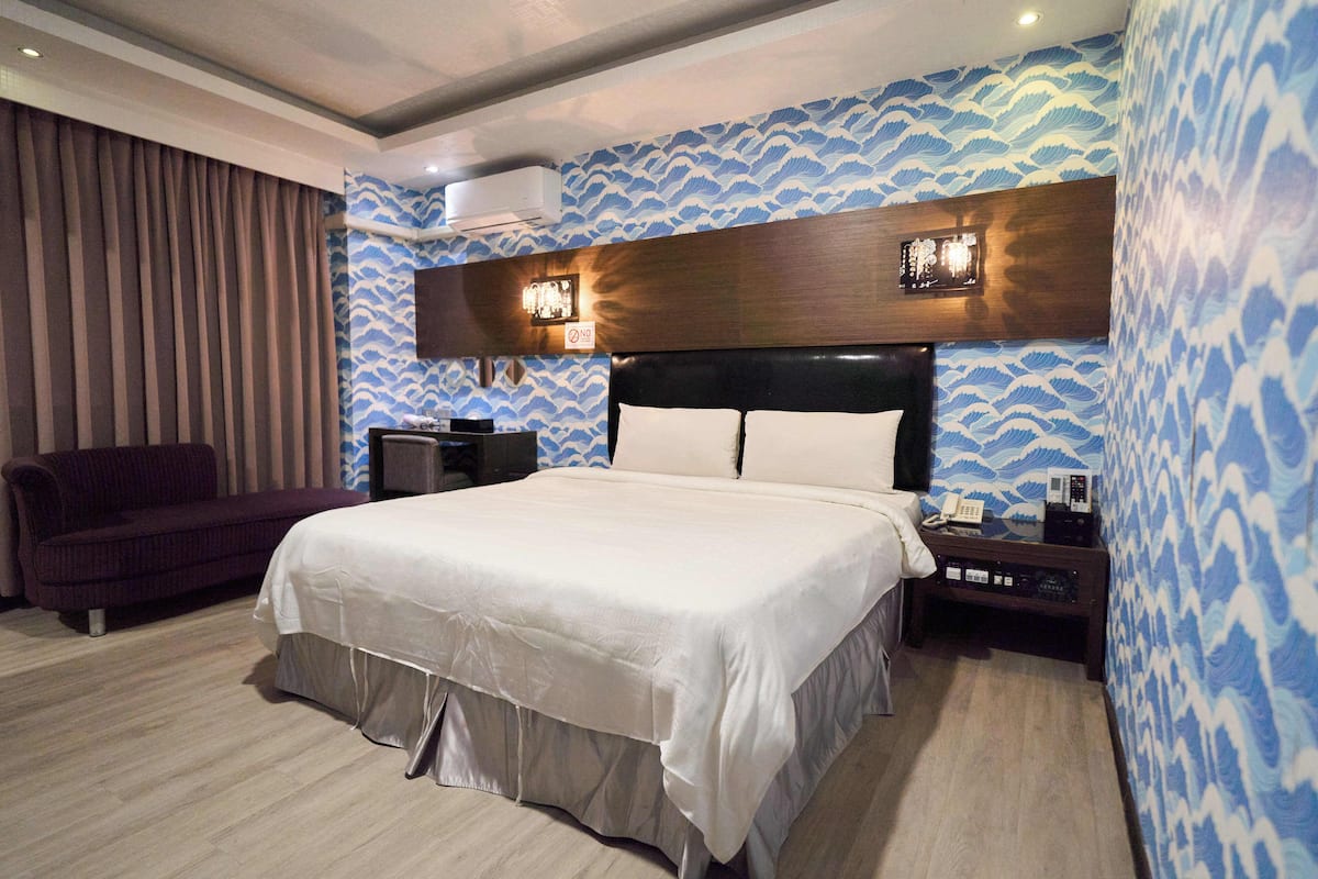 Une chambre d’hôtel comprenant un lit, une table de chevet, un téléphone, un canapé et un mur orné d’un motif ondulé.