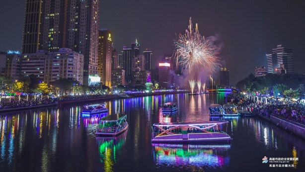Paisatge urbà nocturn amb edificis il·luminats i un espectacle de focs artificials sobre un riu.