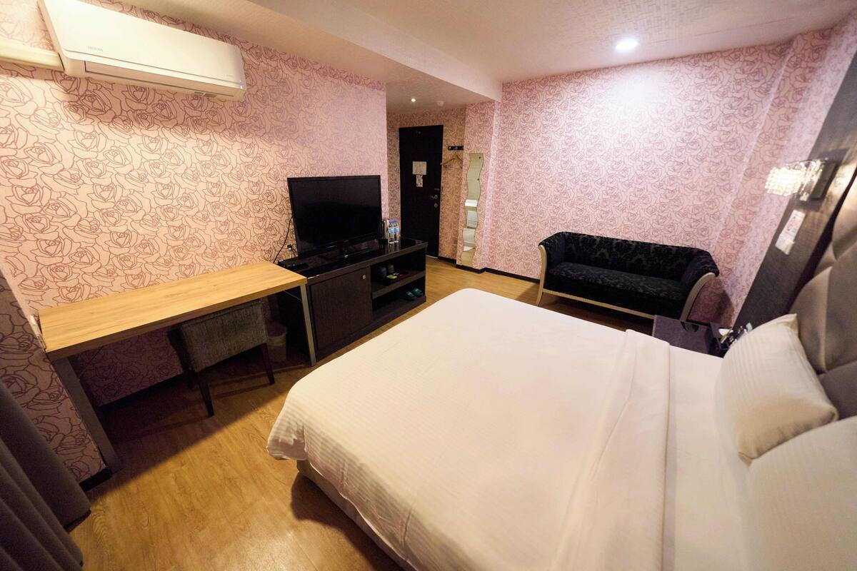 Une chambre d’hôtel équipée d’un lit, d’un bureau avec une télévision, d’un canapé et d’un appareil de climatisation.