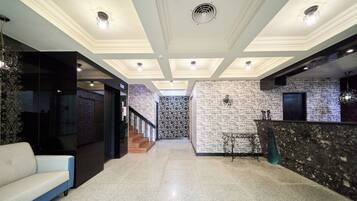 A hotel lobby with a modern design, featuring a reception desk, a staircase, and a seating area.