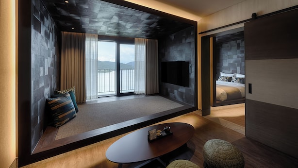 Una habitación de hotel moderna con un ventanal grande, un televisor de pantalla plana, un sofá, una mesa de centro y una cama.