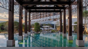 Zona de piscina con una estructura de pérgola de madera, agua cristalina y vistas a un edificio moderno con múltiples balcones.