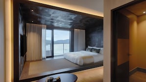 A modern hotel room with a large bed, a view of the outdoors, a wooden floor, and a small round table with a tray of items. - Sono Calm Gyeongju (Gyeongju)