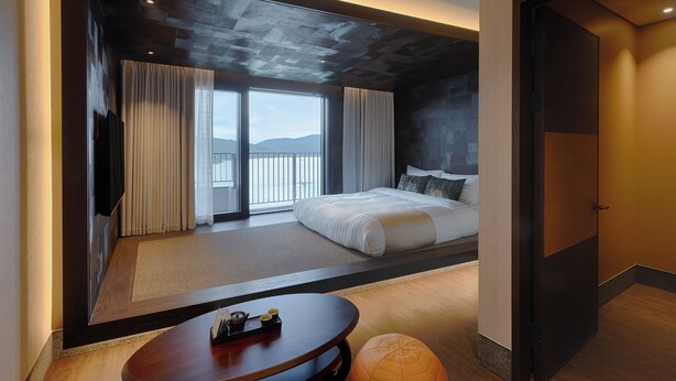 A modern hotel room with a large bed, a view of the outdoors, a wooden floor, and a small round table with a tray of items. - Sono Calm Gyeongju (Gyeongju)
