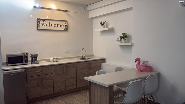Eine moderne Küche mit Mikrowelle, Kaffeemaschine und Spüle. An der Wand hängt ein Schild mit der Aufschrift 'welcome' und auf der Arbeitsfläche steht eine rosa Flamingo-Dekoration.