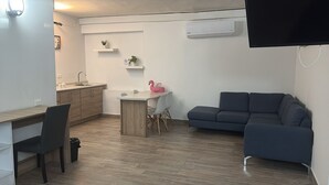 Ein kompakter Wohnbereich mit Küchenzeile, Essplatz, einer Couch und einem an der Wand befestigten Fernseher.