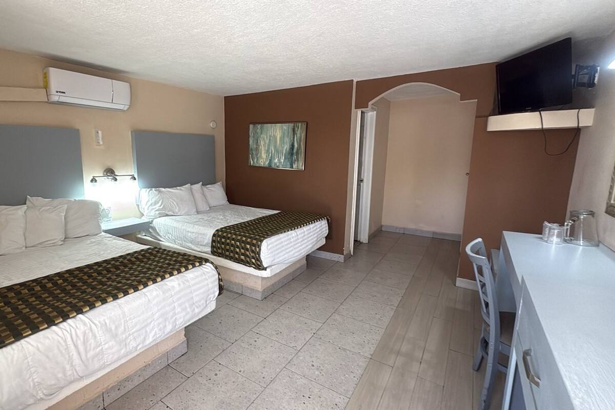 Une chambre d’hôtel avec deux lits, une télévision, un bureau et un tableau au mur.