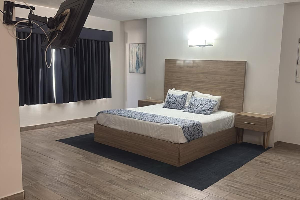 Une chambre à coucher avec un lit en bois, une table de chevet, un bureau, une fenêtre avec des rideaux et des œuvres d’art accrochées aux murs.