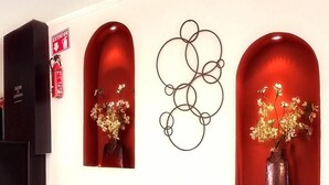 Ein Flur mit roten, bogenförmigen Nischen, die Vasen mit Blumen, einen schwarzen Schrank und ein abstraktes Kunstwerk an der Wand enthalten.