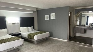 Ein Hotelzimmer mit zwei Betten, einem Badezimmer mit Spiegel und einer grauen Wand.