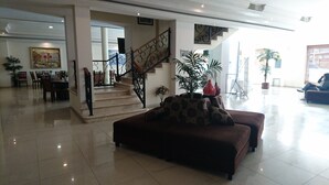 Amplia sala de estar con escalera, comedor y zona de estar con sofá y plantas en macetas.