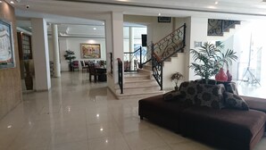 Un vestíbulo amplio con piso pulido, una escalera con barandillas ornamentadas y un área de comedor al fondo.