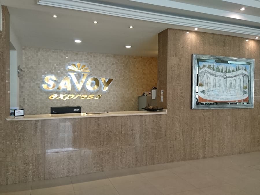 A reception desk with a sign reading "SAVOY Express" and a framed painting of a fountain.