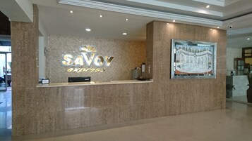 Uma mesa de recepção com uma placa indicando "SAVOY Express" e um quadro com uma fonte.