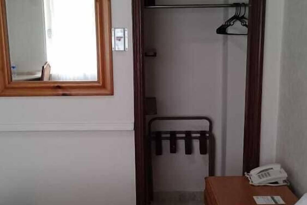 Ett hotellrum med en säng, en garderob i trä, en klädställning, en spegel och en luftkonditioneringsanläggning.