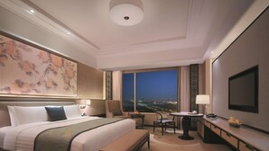 A hotel room with a large bed, a desk, a chair, a view of the city at night, and a television. - Shangri-La Yangzhou (Yangzhou)