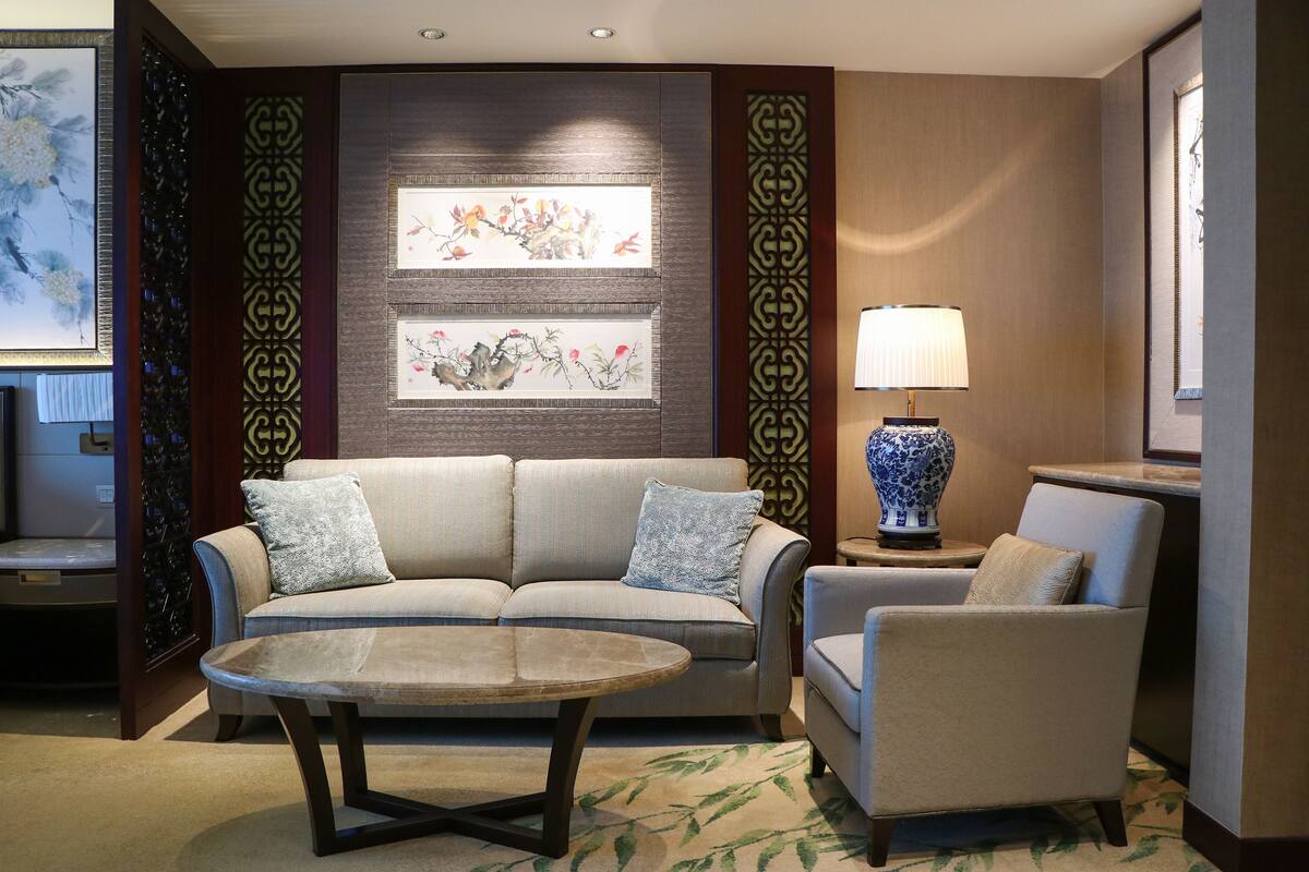 Un salon moderne avec un canapé, un fauteuil et une table basse. Un mur décoratif est agrémenté d’œuvres d’art encadrées, et une lampe est posée sur une table d’appoint.