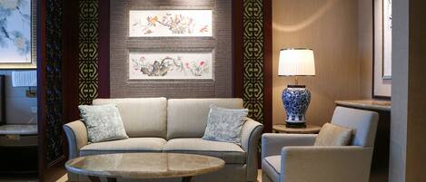 Una sala de estar moderna con un sofá, un sillón y una mesa de centro. Hay una pared decorativa con obras de arte enmarcadas y una lámpara sobre una mesita auxiliar.
