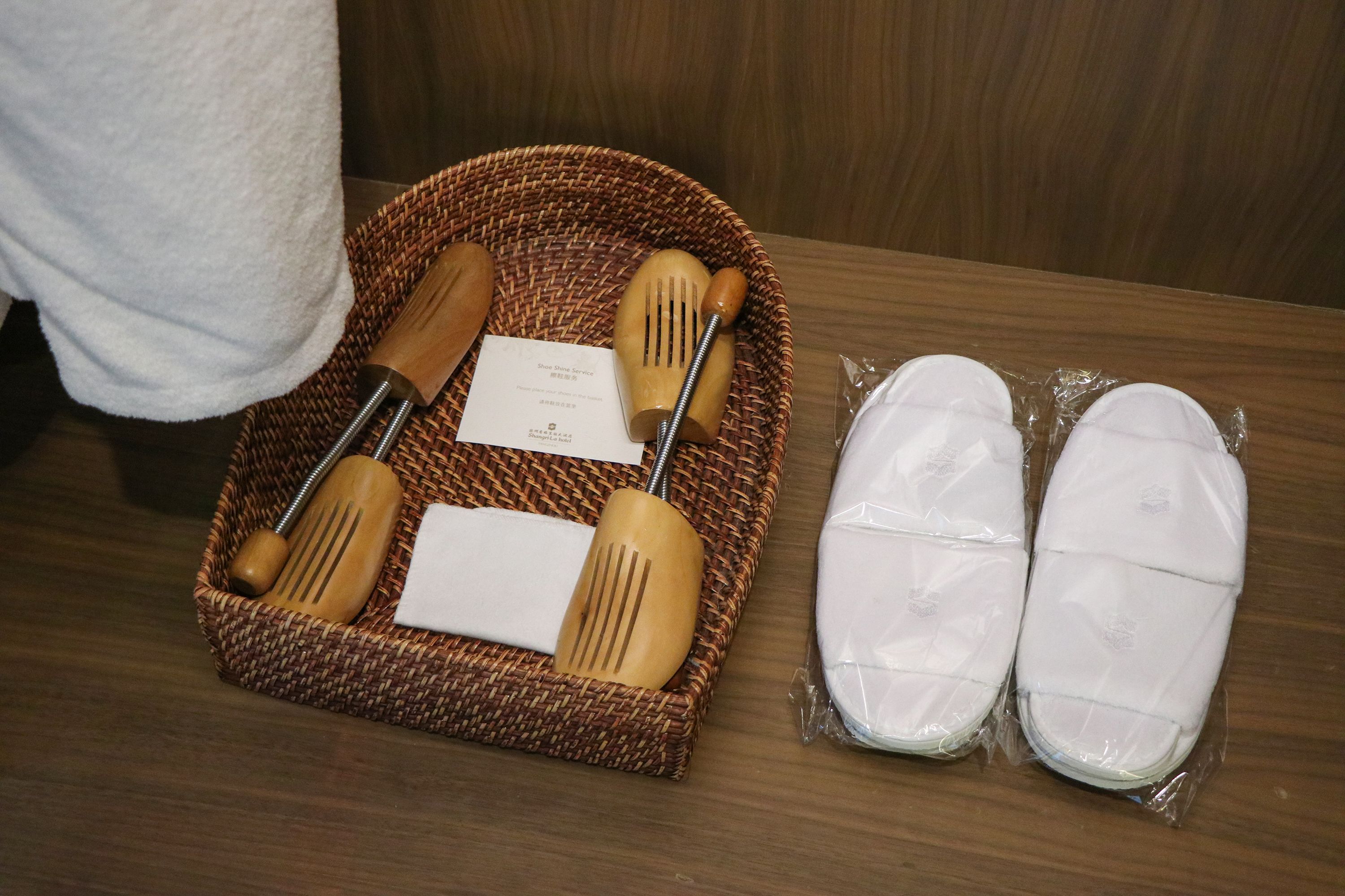 Un panier en osier contenant des ustensiles de cuisine en bois et une serviette, ainsi qu’une paire de pantoufles blanches.