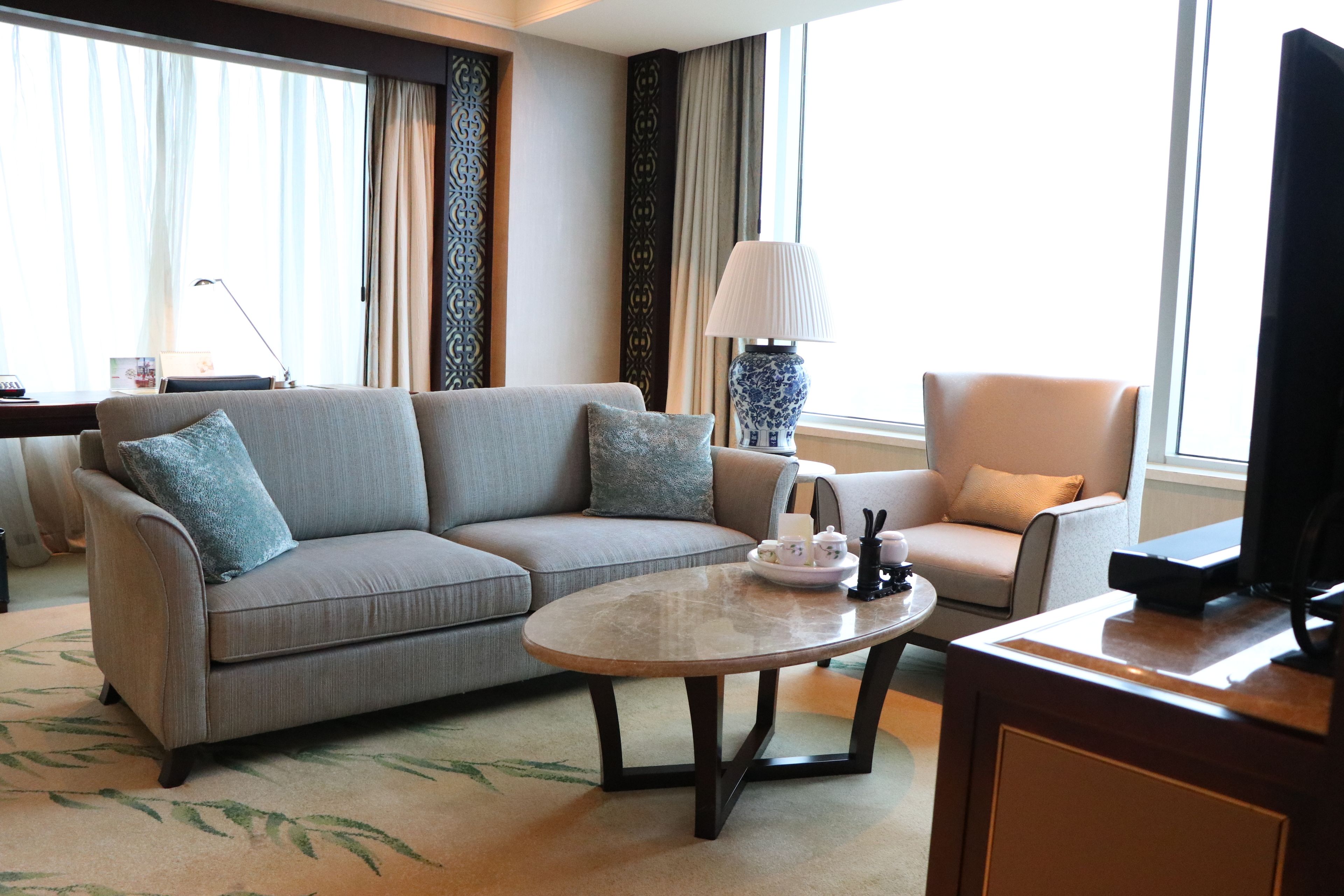 Una habitación de hotel moderna con un sofá gris, una mesa de centro redonda, un televisor y una silla.