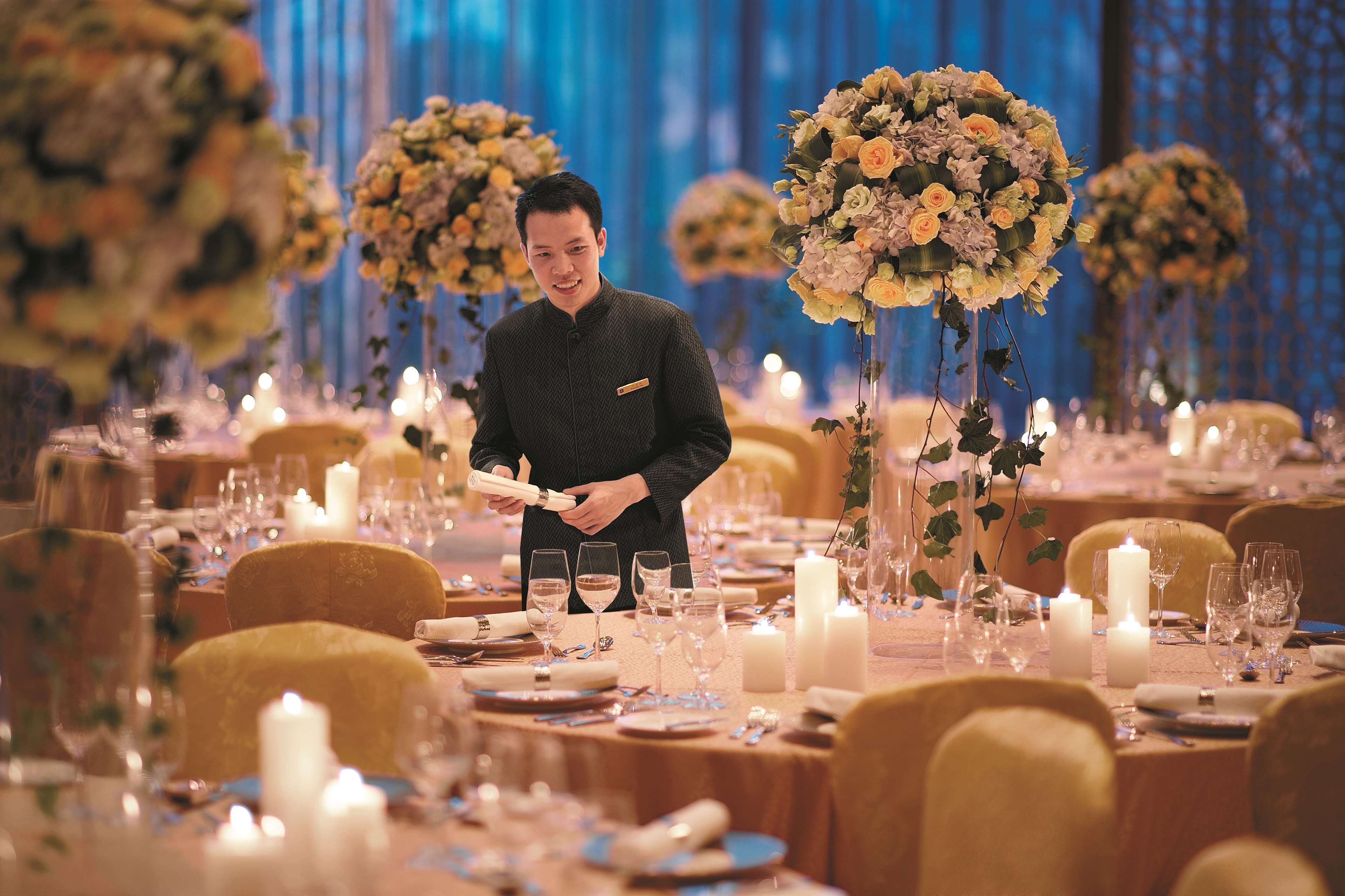 Une salle de banquet avec des tables rondes dressées pour un événement formel, agrémentées de compositions florales et de bougies.