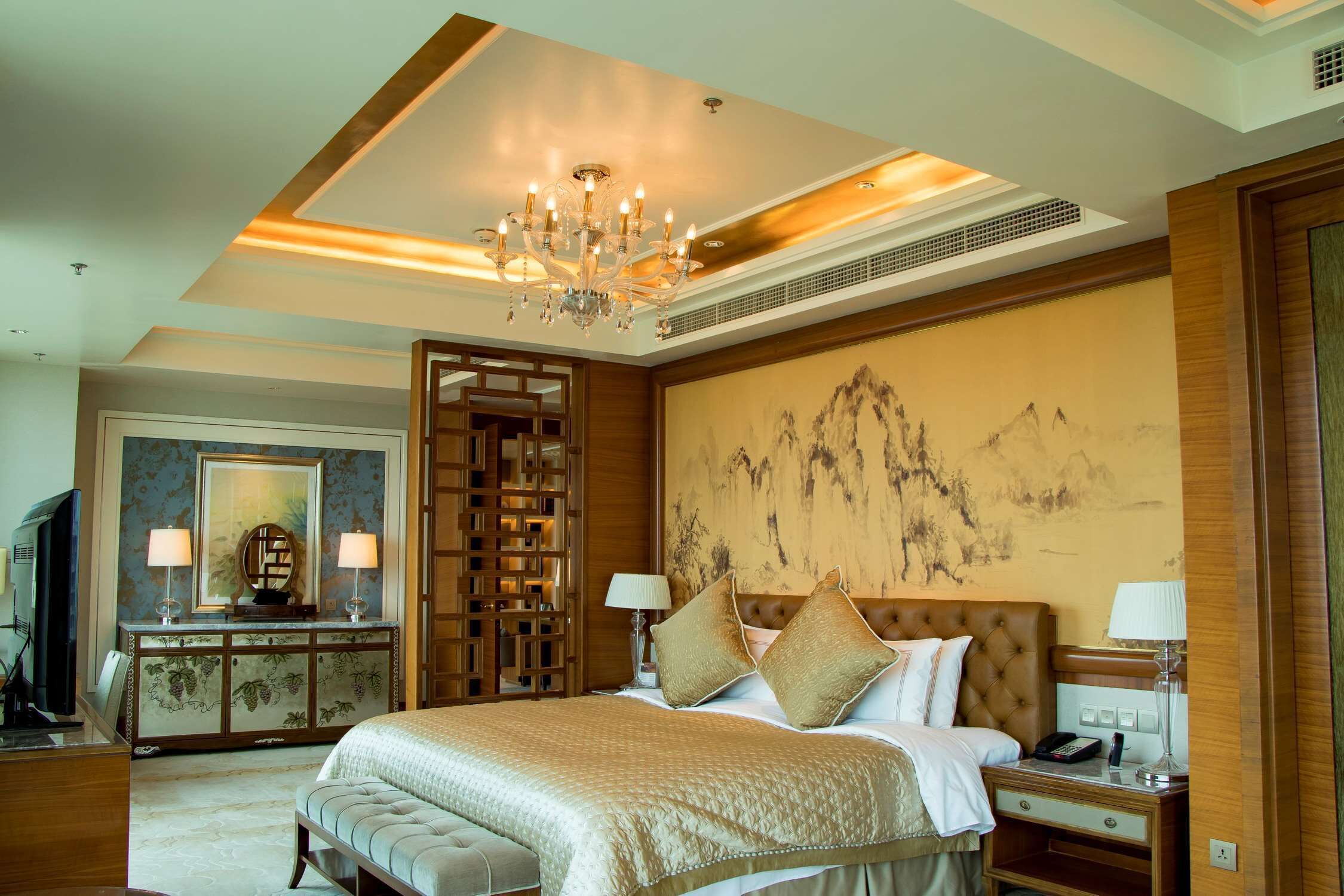A hotel room with a large bed, a television, a desk with a lamp, and a decorative wall piece.
