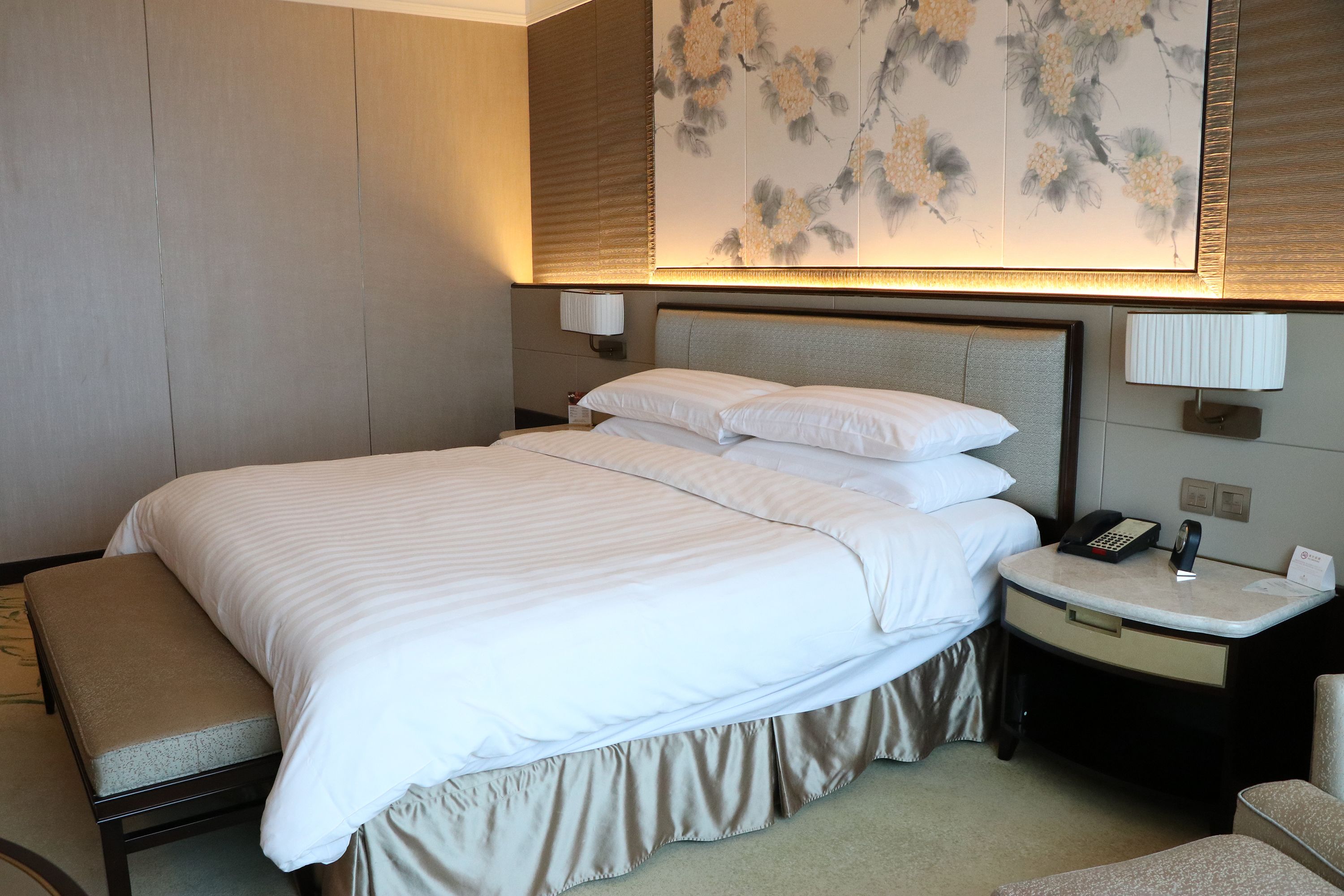 A hotel room with a large bed, a bedside table with a lamp, a telephone, and a wall-mounted artwork.