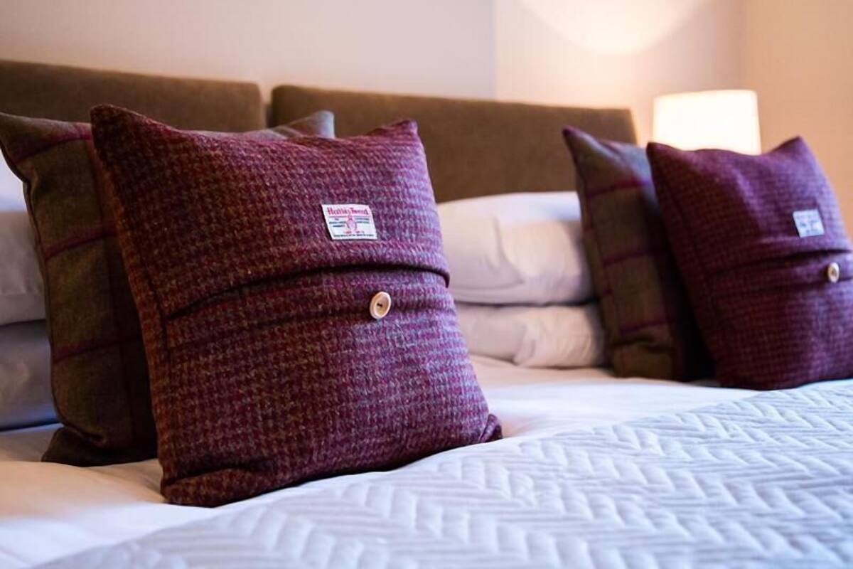 A bed with a patterned bedspread and three pillows with a tag on them.