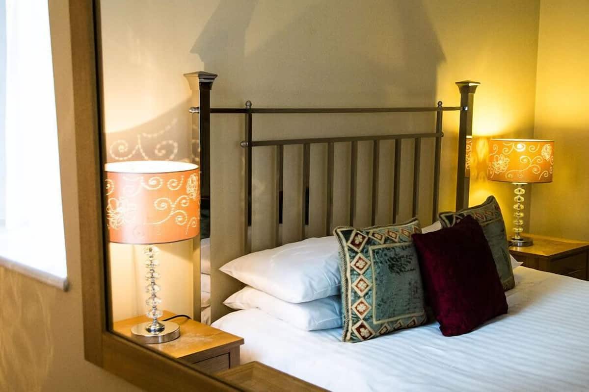 A neatly made bed with white linens and decorative pillows, two bedside lamps with patterned shades, and a wooden nightstand.