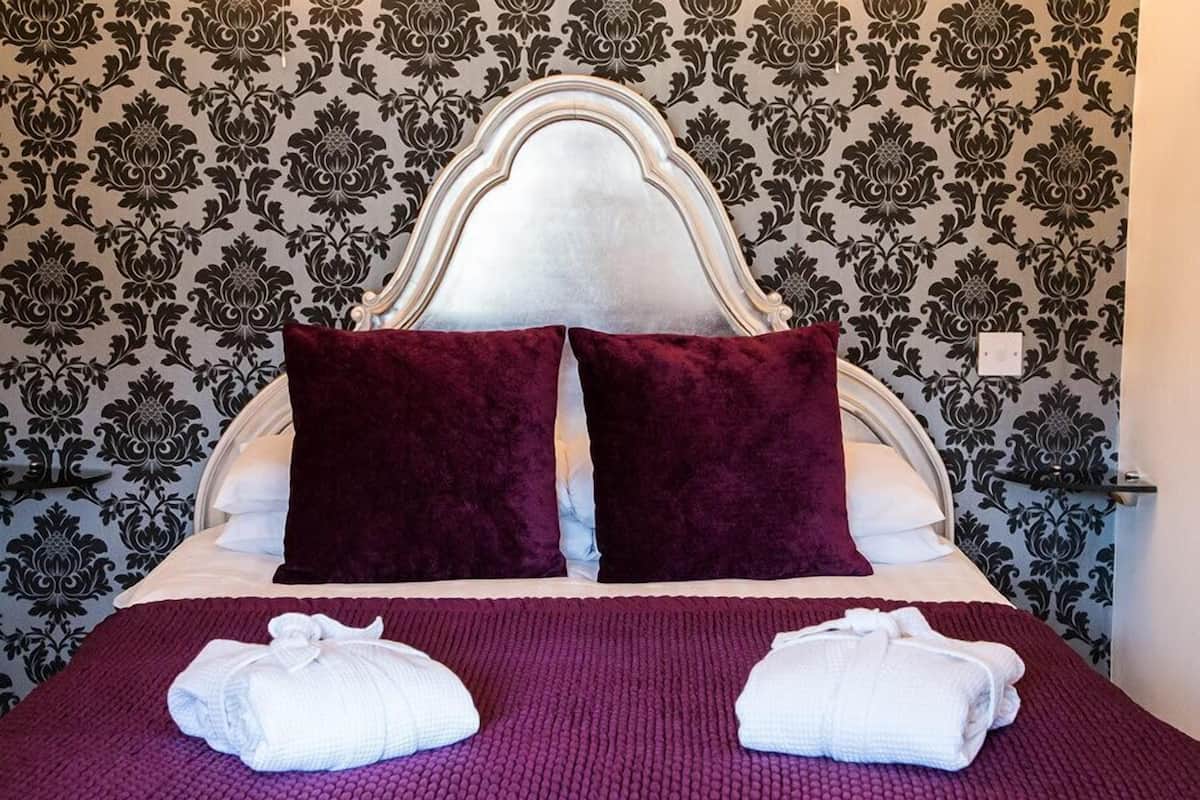 A neatly made bed with a white headboard, two dark red pillows, and two folded white towels.