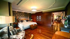 Quarto de hotel com uma cama grande, área de estar com um sofá, piso de madeira e um candelabro.