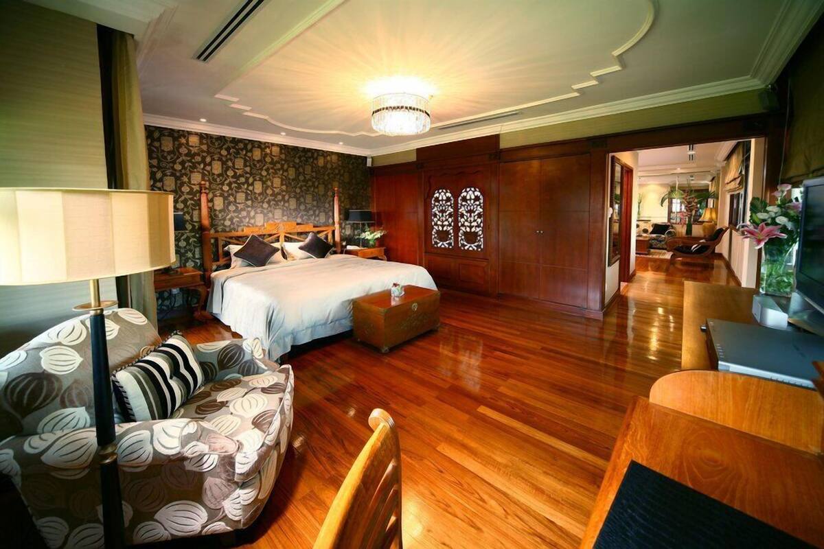 Une chambre d’hôtel avec un grand lit, un coin salon avec un canapé, un parquet et un lustre.