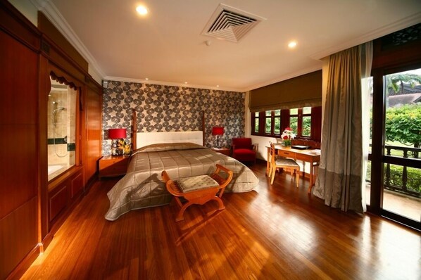 Un dormitorio amplio con una cama grande, un escritorio de madera y vistas a la vegetación por la ventana.