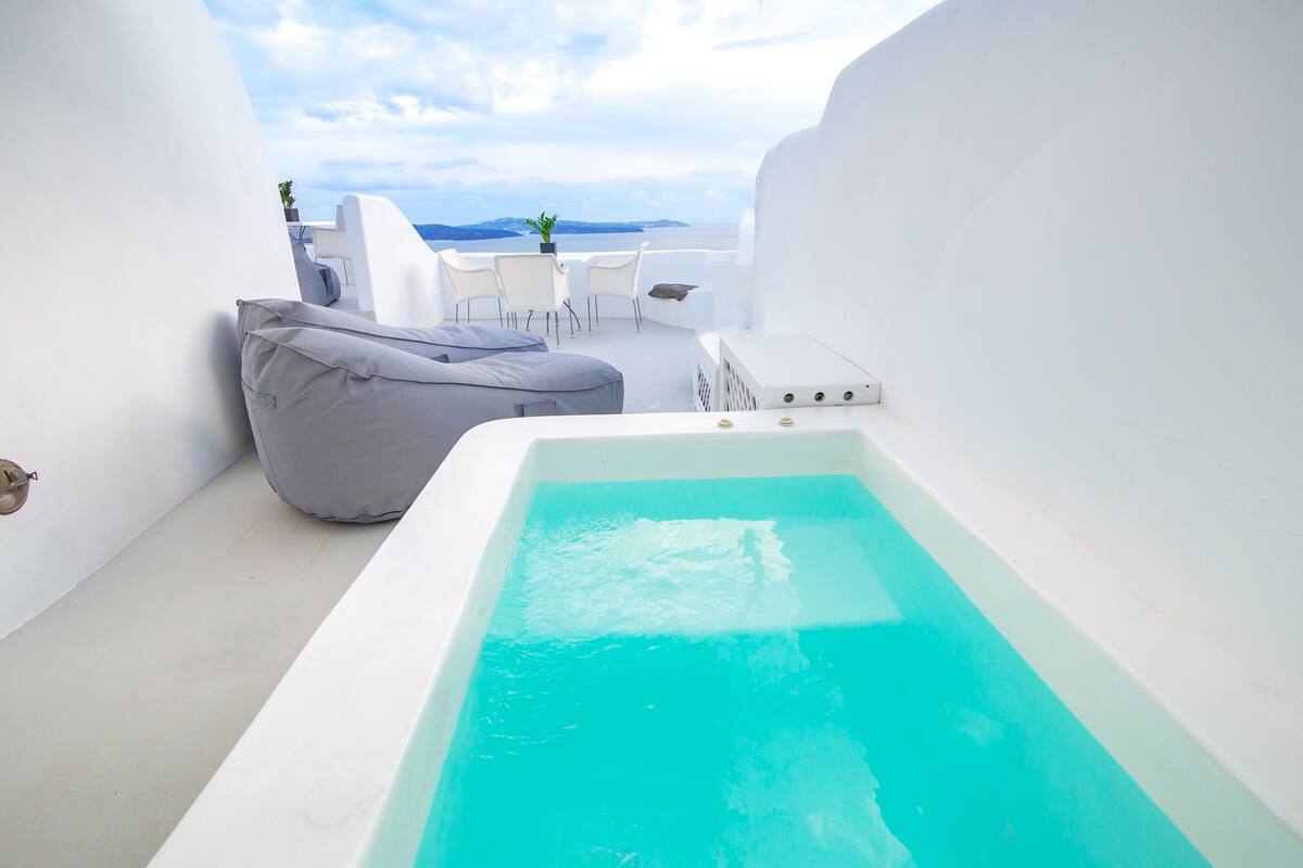 A modern outdoor pool area with a white infinity pool, a gray bean bag chair, and a white table with chairs.