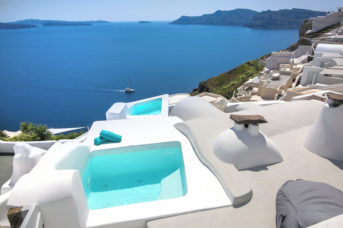 A seaside hotel with white architecture, a pool, and a view of the sea.