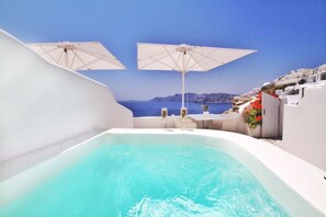 A pool area with two white umbrellas, a hot tub, and a view of the sea and white buildings. - Onar Villas Oia - Onar Hotels Collection (Santorini)