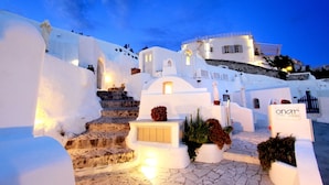 A white-washed building with a staircase leading to a door, surrounded by stone steps and potted plants. - Onar Villas Oia - Onar Hotels Collection (Santorini)